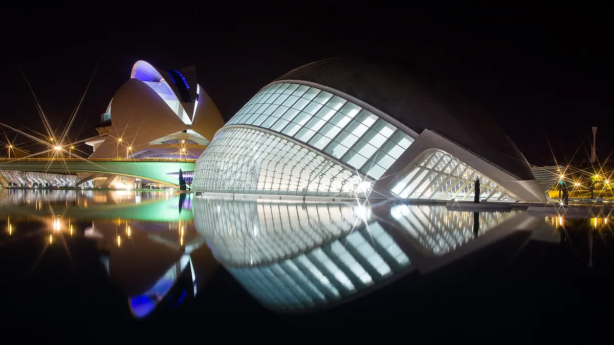 The glass-and-steel buildings of the City of Arts and Sciences lit at night, reflected in a still pool in Valencia