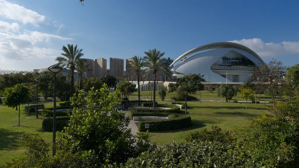 Palm trees, lawns and paths in the Turia Garden in Valencia, with the curved white roof of the opera house behind the trees